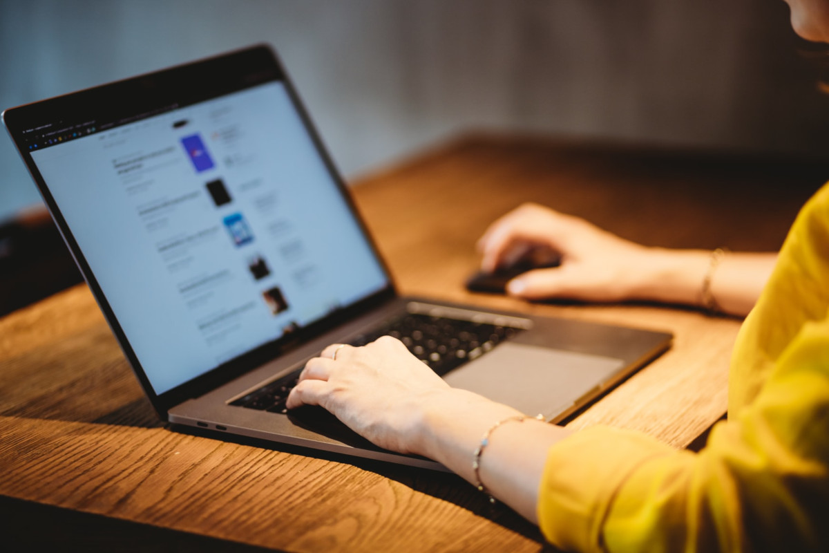 Close up of laptop computer being used by woman in yellow sweater sitting at wooden desk.